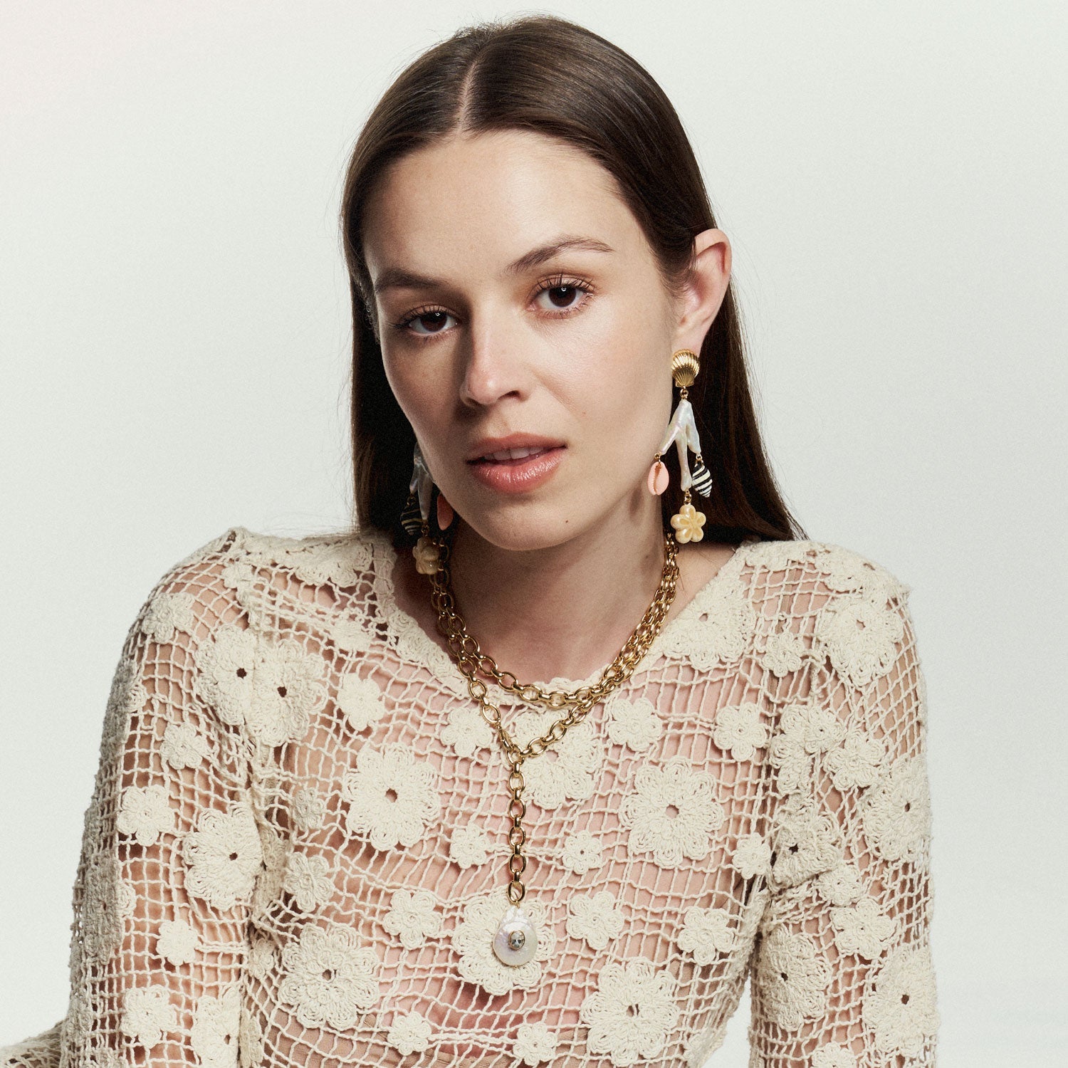 Woman wearing a lace top and gold jewelry against a plain background